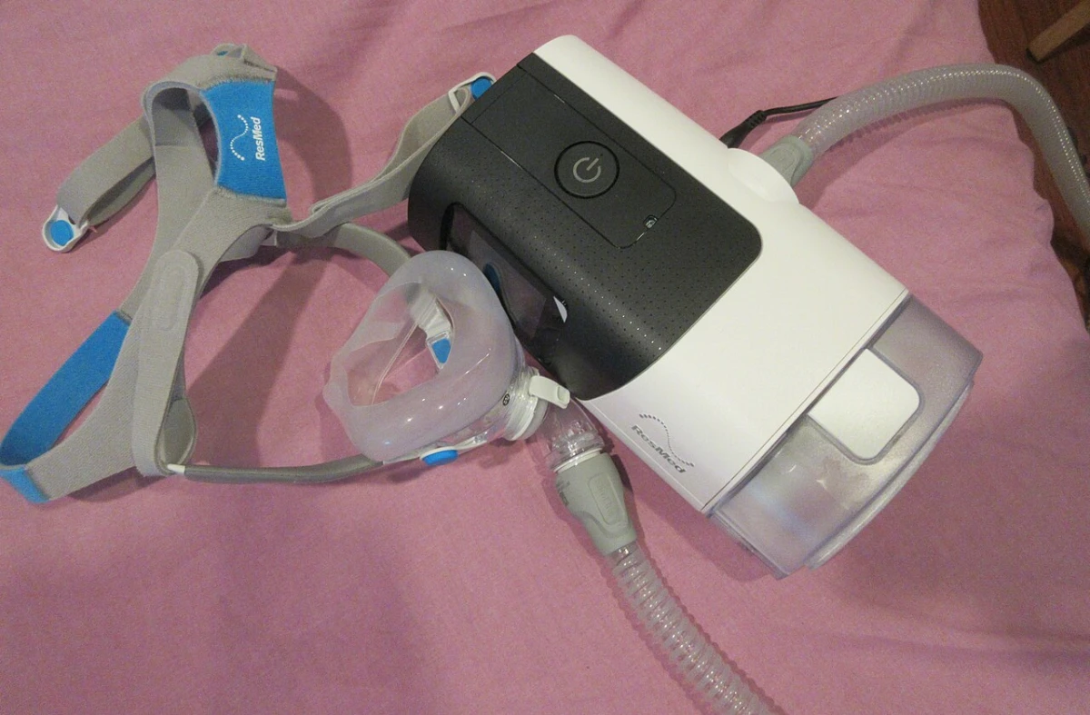 A CPAP machine with its full face mask, headgear straps and hose lying on a bed